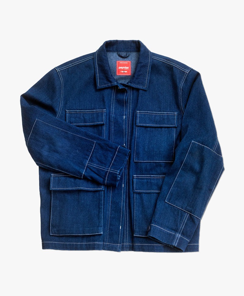 A dark indigo denim jacket with square elbow patches, square pockets with flaps, white contrast top-stitching, and a hidden button placket. The jacket has a hanging loop and a red label that says "Paynter" at the collar.