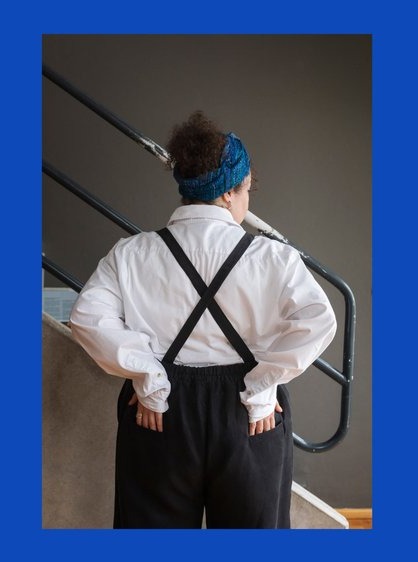 Back view of a person wearing overalls with crossed back straps. Hands are on lower back.