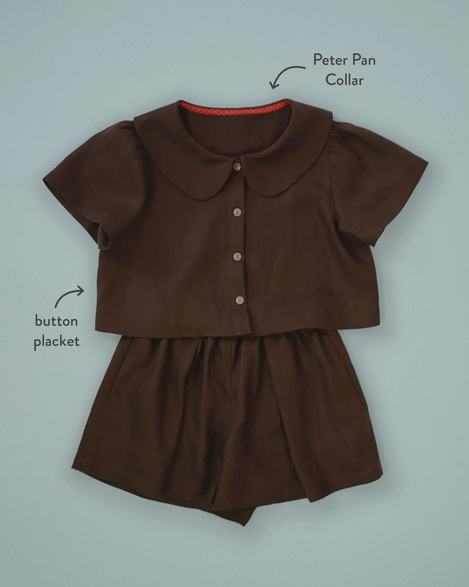 Flat lay of a brown short-sleeved blouse and shorts set. The blouse has a button placket and a Peter Pan collar (labeled on photo).