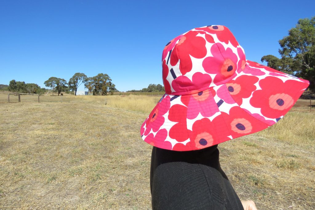 Image of person wearing an example of the low waste sunhat in a red/white floral fabric. 