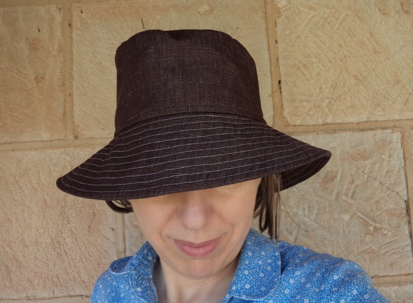 Image of a person wearing a bucket hat made in a brown fabric with stitching in a contrasting thread. 