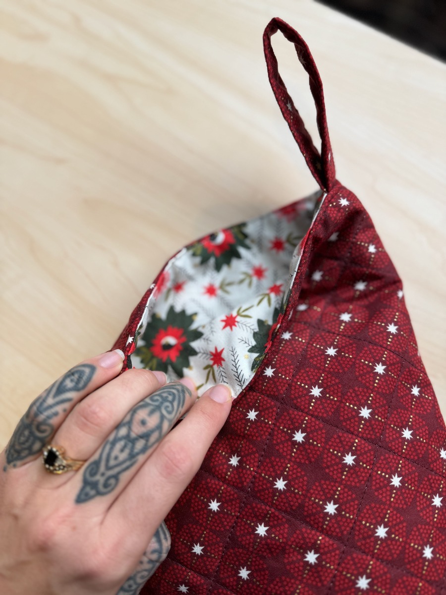 A hand with finger tattoos folds over the top edge of the red stocking to reveal the white contrast lining.